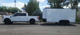White Ford F-150 towing a large enclosed cargo trailer in a full side view on a residential street.