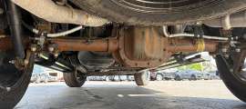 Close-up under a Ford F-150 XLT showing rust on the rear axle and differential while parked on a dealer lot.
