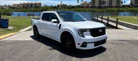 White Ford Maverick parked beside a waterfront boat ramp in a front three-quarter view.