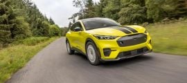 Yellow Ford Mustang Mach-E Rally electric SUV kicking up dust while driving on a gravel dirt road