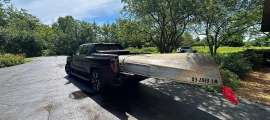 Black GMC Sierra EV towing a canoe on a small trailer in a residential driveway.