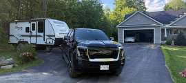 Black GMC Sierra EV parked in a driveway while towing a Winnebago Micro Minnie camper trailer.