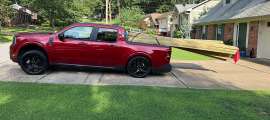 Red Ford Maverick parked in a driveway with long lumber extending from the truck bed.