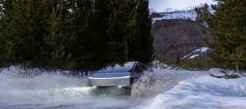 Tesla Cybertruck driving through a snowy water crossing and throwing up a large splash in a winter forest.