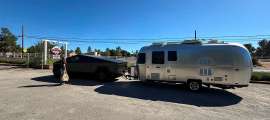 Tesla Cybertruck towing an Airstream travel trailer in a parking lot with a person standing beside the truck.