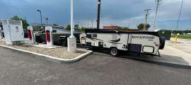 Tesla Cybertruck towing a Rockwood travel trailer while parked at a Tesla Supercharger station