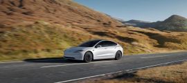 White Tesla Model 3 driving on a scenic highway through rolling hills, emphasizing electric range and minimalist design.