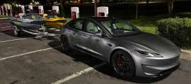 Tesla Model 3 towing two Sea-Doo personal watercraft on a trailer at a Tesla Supercharger station at night.