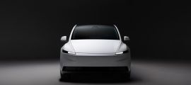 White Tesla Model Y front view in a dark studio setting, highlighting minimalist design and LED headlights