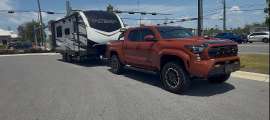 Toyota Tacoma towing an Outback travel trailer in a front three-quarter view near an intersection.