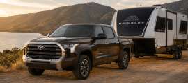 Dark brown Toyota Tundra towing a black and white Brinkley travel trailer beside a lake at sunset