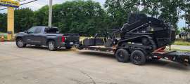 Gray Toyota Tundra towing a large equipment trailer with a black skid steer loaded on it.