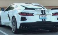 A white 2023 Chevrolet Corvette C8 with black racing stripes shown from the rear three-quarter view, featuring distinctive LED taillights and a Kentucky license plate.
