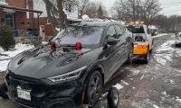 A black Ford Mustang Mach-E electric SUV, likely a 2022 model, is shown being loaded onto a tow truck from its front three-quarter angle on a snowy residential street.