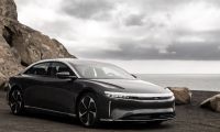 2023 Lucid Air luxury electric sedan in gray, front three-quarter view parked along a rocky coastal cliff with ocean backdrop.
