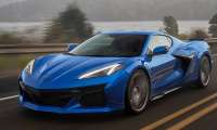 Blue 2023 Chevrolet Corvette Z06 driving on a country road at sunset in a front three-quarter action view.