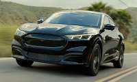 Black 2023 Ford Mustang Mach-E Premium driving on a two-lane road in a front three-quarter action view.