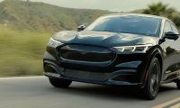 Black Ford Mustang Mach-E driving on a scenic road, front three-quarter view of electric crossover