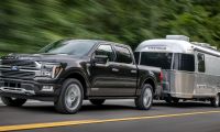 Black 2024 Ford F-150 Platinum towing an Airstream travel trailer, front three-quarter view demonstrating luxury and hauling capability.