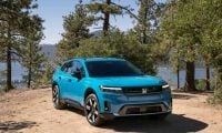 2024 Honda Prologue in bright turquoise blue, front three-quarter view, showcasing sleek LED headlights and modern crossover design, parked on mountain overlook with pine trees and lake vista.