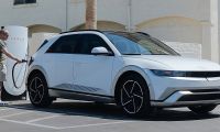 2024 Hyundai Ioniq 5 in white parked at a Tesla Supercharger station with an owner plugging in the NACS charging cable demonstrating the Ioniq 5s expanded charging network access in a sunny suburban parking lot