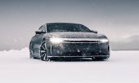 2024 Lucid Air electric sedan driving through snowy landscape in Norway, front view with illuminated LED light strip and winter performance setting.