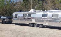 2024 Tesla Cybertruck towing a polished Airstream travel trailer, demonstrating electric truck towing capability and long-distance road travel