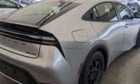 2024 Toyota Prius Prime in silver, rear three-quarter view, featuring black alloy wheels and distinctive fastback design, parked under dealership canopy.