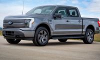 2024 Ford F-150 Lightning Flash trim in gray parked on a paved road with a grassy field and blue sky in the background.