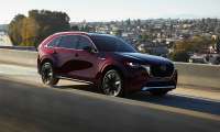 Red 2024 Mazda CX-90 driving on a highway in a front three-quarter action view.