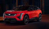 2025 Cadillac Optiq Sport in infrared red with a gloss black roof posed under dramatic nighttime lighting with sharp angular LED headlights glowing highlighting the luxury electric crossover front fascia design