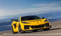 A bright yellow 2025 Chevrolet Corvette Z06 shown from a three-quarter front angle, photographed on a mountain road against a dramatic blue sky backdrop.