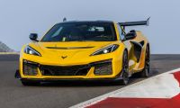 2025 Chevrolet Corvette Z06 in yellow driving aggressively on a race track, shown from a dynamic front angle with a large rear wing.