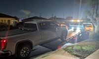 2025 GMC Sierra AT4 pickup truck in silver being loaded onto a tow truck at night in a residential neighborhood, illuminated by service lights.