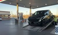 Black 2025 GMC Yukon being loaded onto a flatbed tow truck at a gas station during sunset.