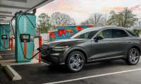 Dark gray Genesis GV70 SUV parked at Ionna charging station during sunset with vibrant pink and orange sky