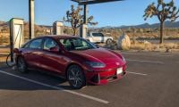 Red 2025 Hyundai Ioniq 6 electric sedan parked at charging station in Joshua Tree desert, mountains visible, three-quarter front view.