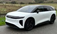 2025 Lucid Gravity electric SUV in pearl white, shown at three-quarter front angle on rural mountain road, featuring sleek aerodynamic design and black contrast elements.