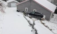 Black Ford Mustang Mach-E parked on a snowy driveway beside a house, showing winter driving conditions and snow-covered landscape.