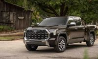 2023 Toyota Tundra Limited in dark brown, front three-quarter view, featuring chrome honeycomb grille and LED headlights, parked near rustic pottery barn.