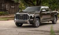 Smoked Mesquite 2025 Toyota Tundra 1794 Edition parked near a rustic building in a front three-quarter view.