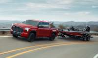 Red 2025 Toyota Tundra towing a fishing boat on a winding road, demonstrating the truck's towing capability.