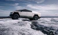 Tesla Cybertruck in stainless steel parked on an icy ridge, showcasing its angular design, off-road tires, and futuristic exterior in a cold landscape.