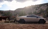 Tesla Cybertruck parked on a rural ranch beside horses and hay bales in a mountainous landscape.