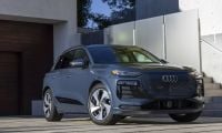 2024 Audi Q4 e-tron in metallic gray, front three-quarter view, parked on modern concrete driveway with geometric white walls.