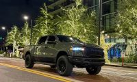 2026 Dodge Ram pickup truck in matte green parked on illuminated city street at night with modern buildings and decorative lights