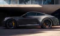Gray 2026 Porsche 911 Carrera parked outside a modern home with large yellow brake calipers and black wheels.