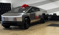 2026 Tesla Cybertruck RWD front three-quarter view indoors with a red bow on the roof, showcasing stainless steel body and angular electric pickup design.