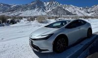 2026 Toyota Prius hybrid front three-quarter view in white driving through snowy mountain landscape