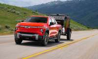 A red Chevrolet Silverado EV Trail Boss towing a small trailer on a mountain highway.